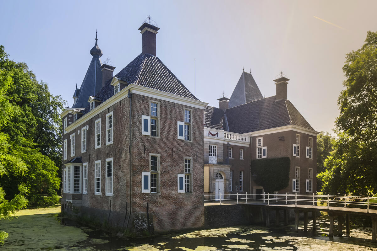 Kasteel het Nijenhuis met de loopbrug en omringd met water. De lucht is blauw.