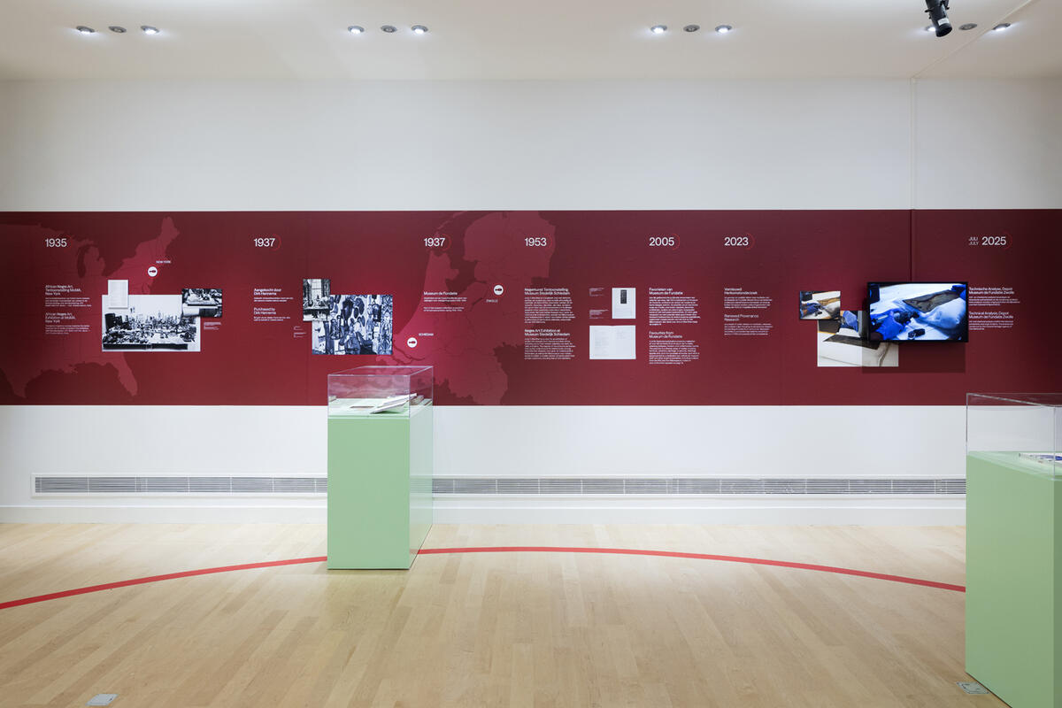Eine Wand des Museums mit einem roten Streifen darauf. Auf diesem Streifen befinden sich alle Informationen und Fotos aus der Provenienzforschung von Back to Benin.