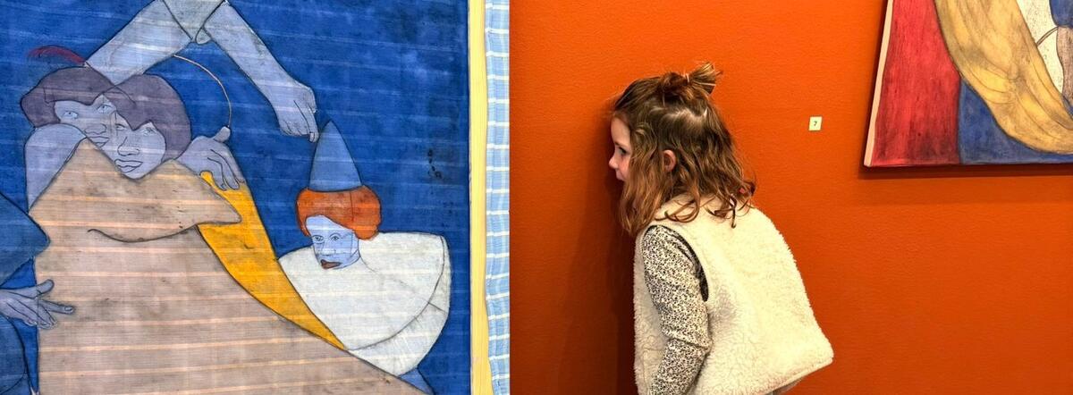 Ein kleines M&auml;dchen steht mit dem Gesicht an einer orangefarbenen Wand. Sie schaut auf die R&uuml;ckseite eines Gem&auml;ldes.