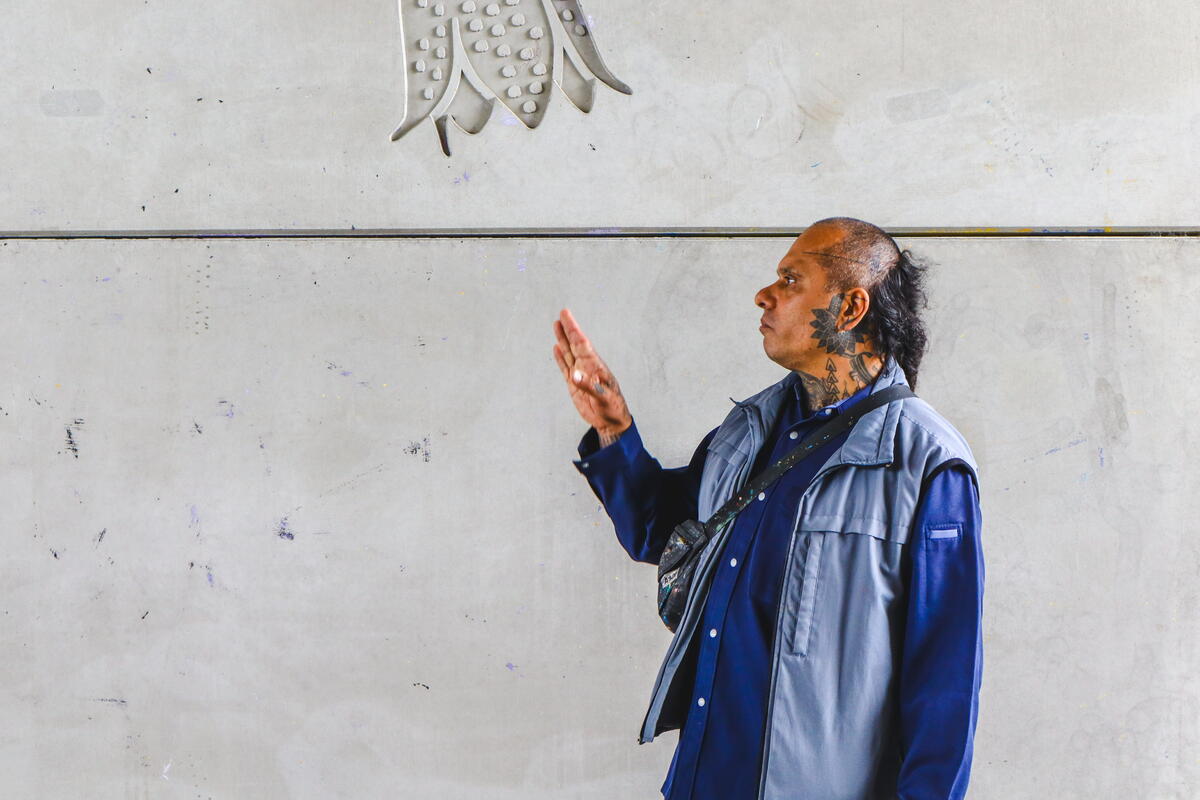 Kunstenaar Kenneth Letsoin staat voor een grijze muur en kijkt omhoog naar het reli&euml;f van een tulp die naar beneden reikt.