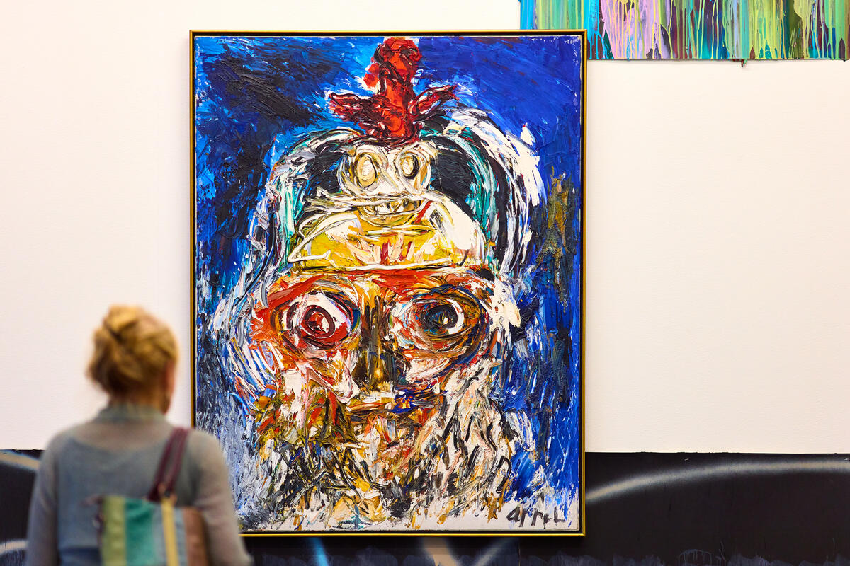 Een vrouw kijkt naar een groot kleurrijk schilderij van Karel Appel.