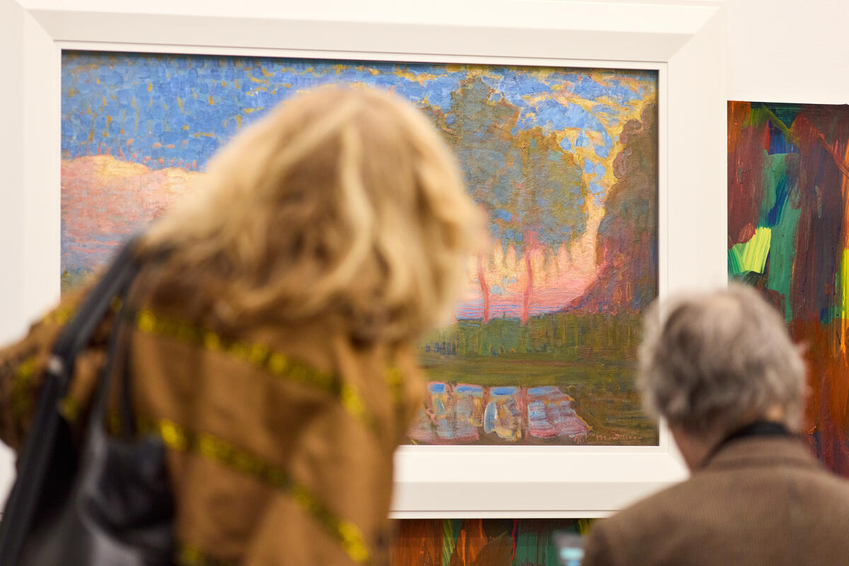Ein Mann und eine Frau betrachten ein impressionistisches Gem&auml;lde mit warmen Farben einer Landschaft.