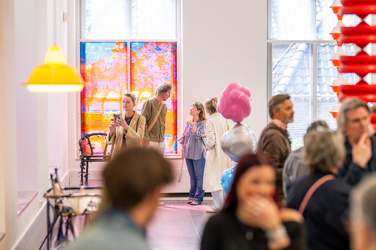 Die Besucher stehen in einem wei&szlig;en Raum mit farbenfrohen Artefakten. Eine Frau macht ein Foto von einem Kunstwerk.