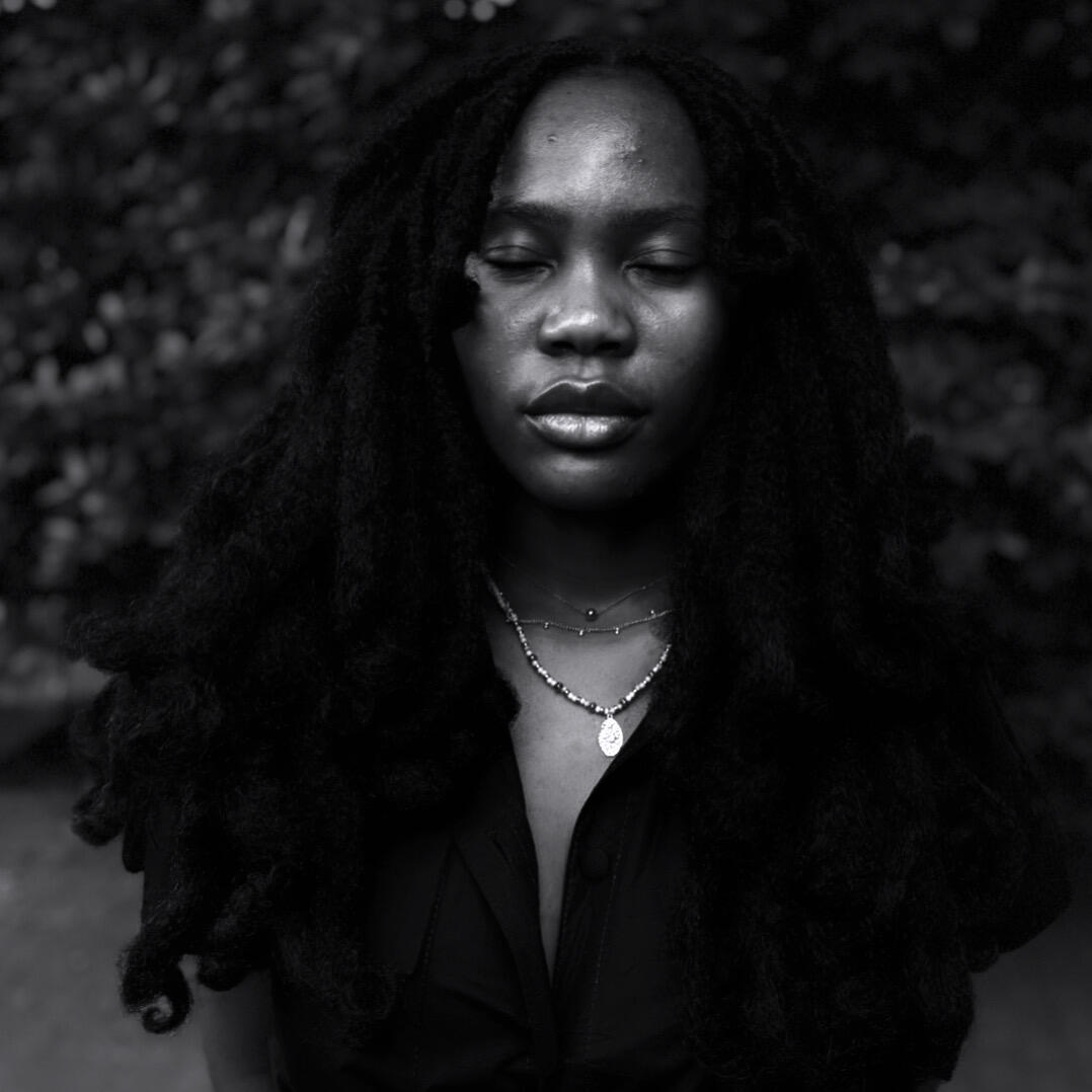 Een zwart-witte portretfoto van Osaru Obaseki. Ze staat op de foto met haar ogen gesloten in een zwarte blouse.