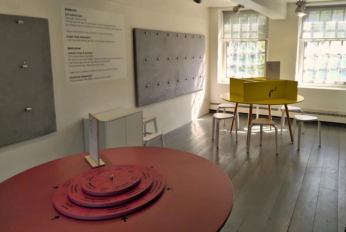Een foto van de studio in Heino. In een knusse ruimte staat een rode ronde tafel met draaischijven erop. Achterin staat een gele tafel met doorkijkjes.