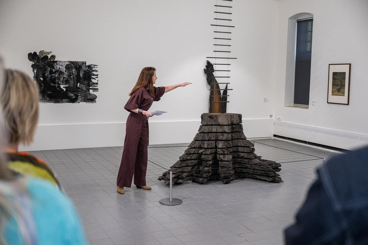 Wilma Wilbrink stands next to her artwork of bog oak and points to this, while an audience listens.