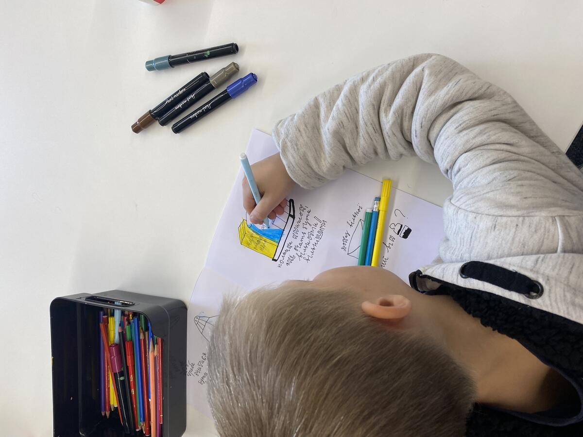 Een jongetje van vier zit aan een tafel en tekent. 