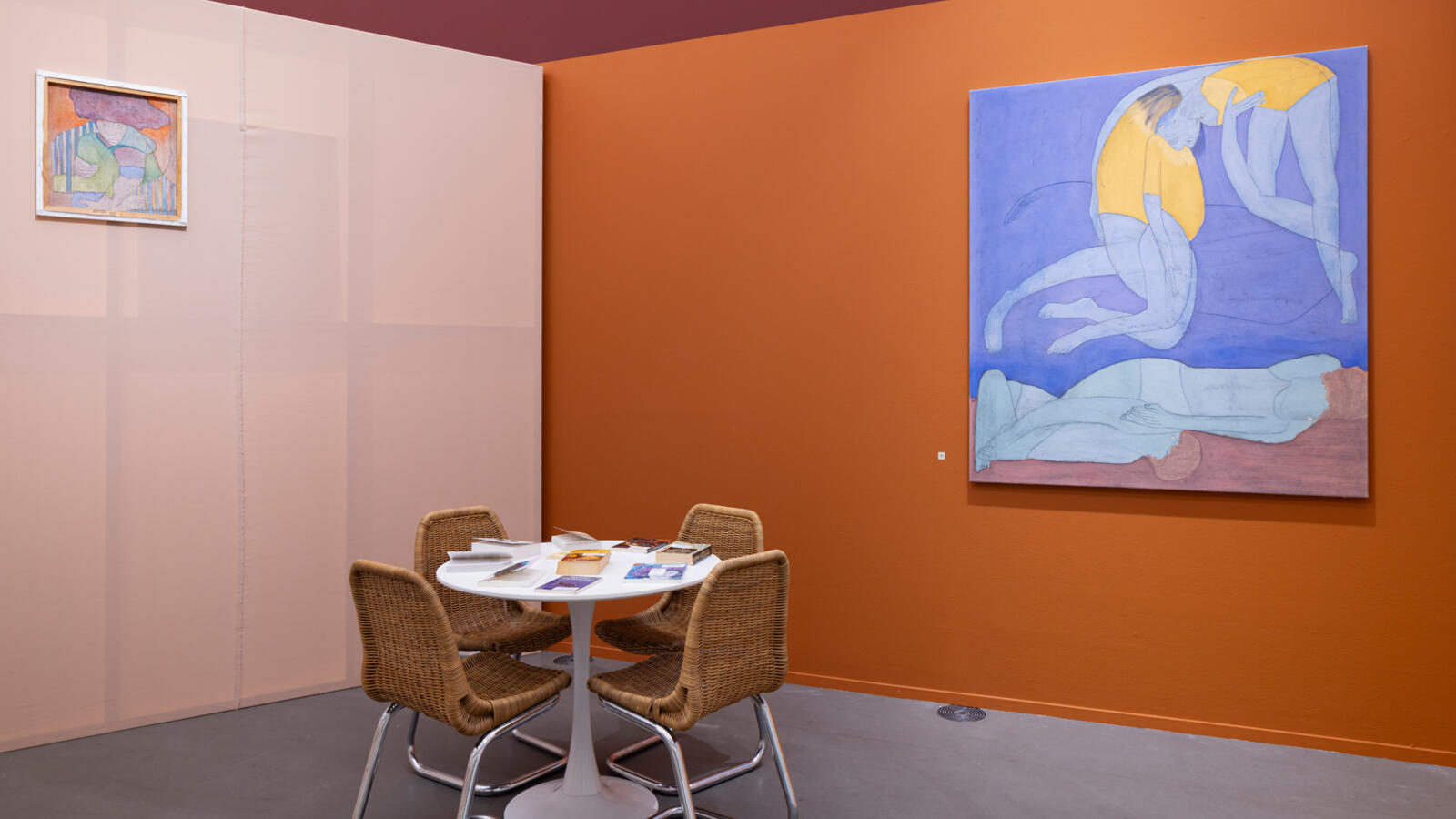 Een ronde tafel staat voor een oranje en lichtroze muur. Een blauw schilderij hangt aan de muur.