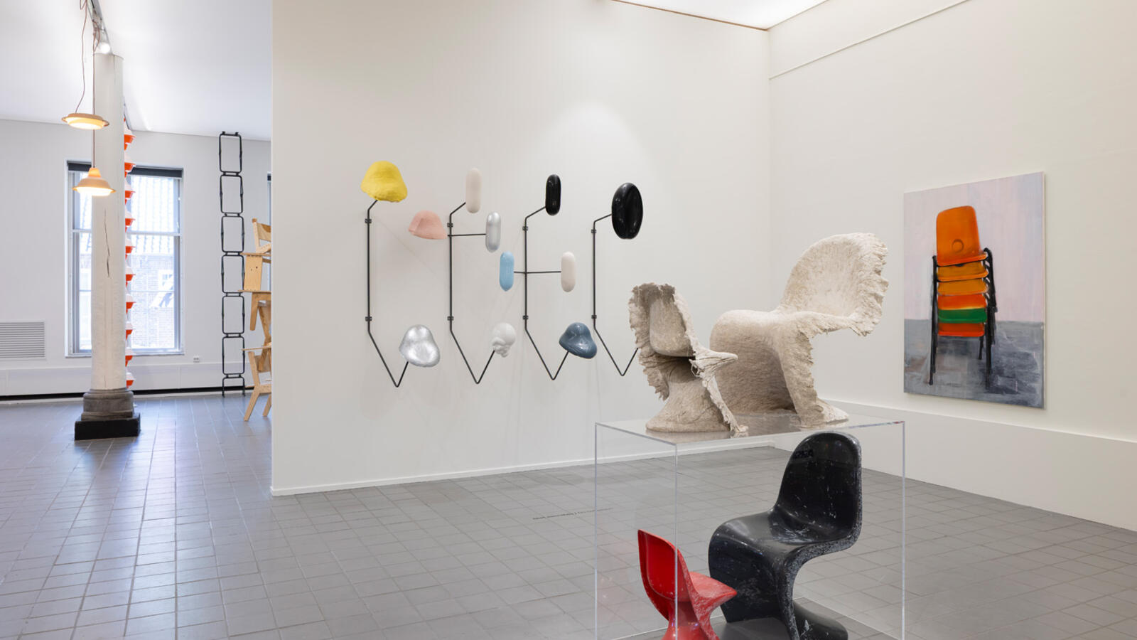 De Panton Imprint Chair van Jack Brandsma staat in de ruimte, met daaronder een versie van de twee stoelen in zwart en rood. Er hangt een schilderij van stoelen op de muur en een kunstwerk van wat mogelijk zadels zijn aan de muur.