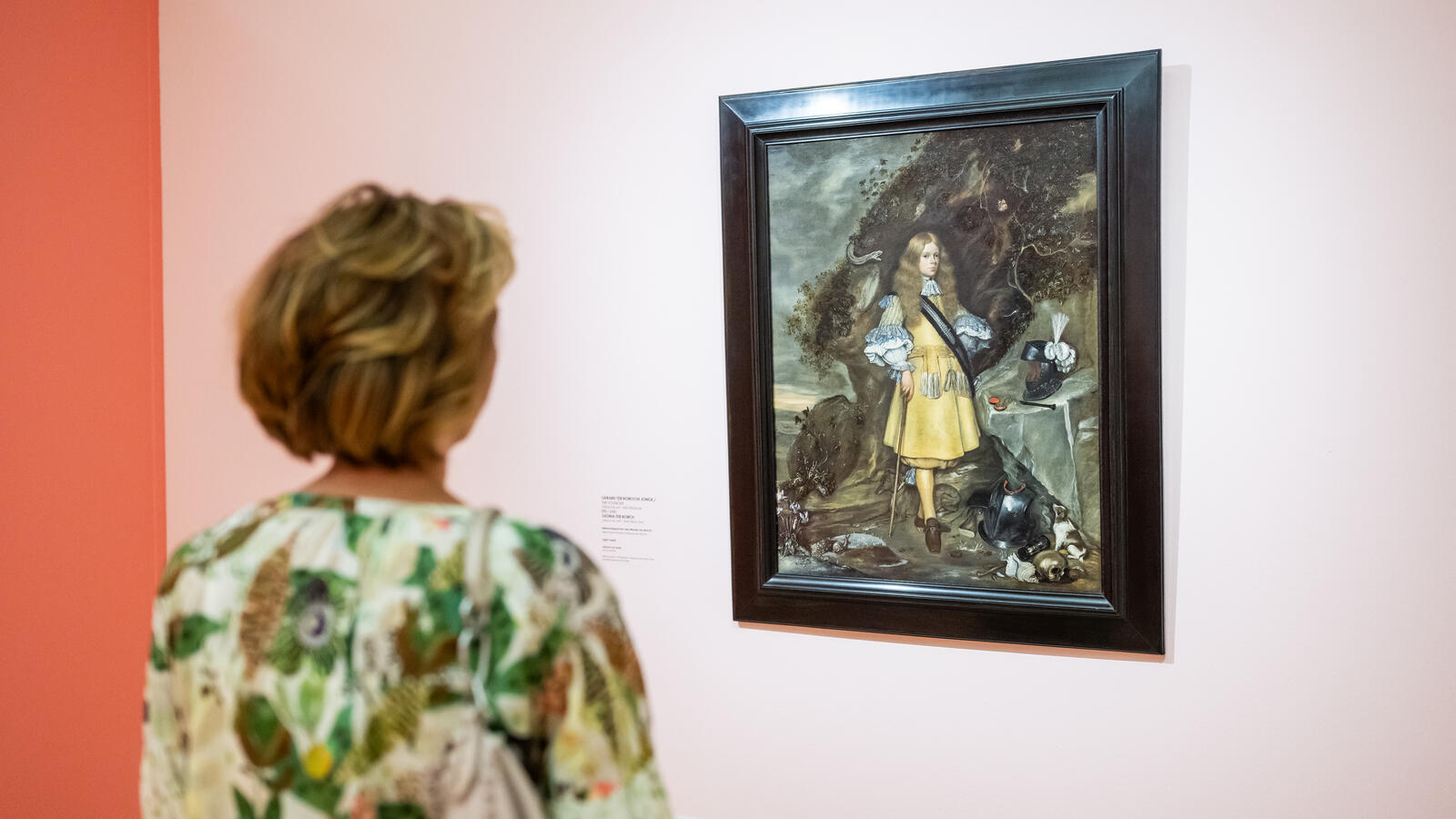 Een vrouwelijke bezoeker staat voor een schilderij van Moses Ter Borch. De muren zijn lichtroze.