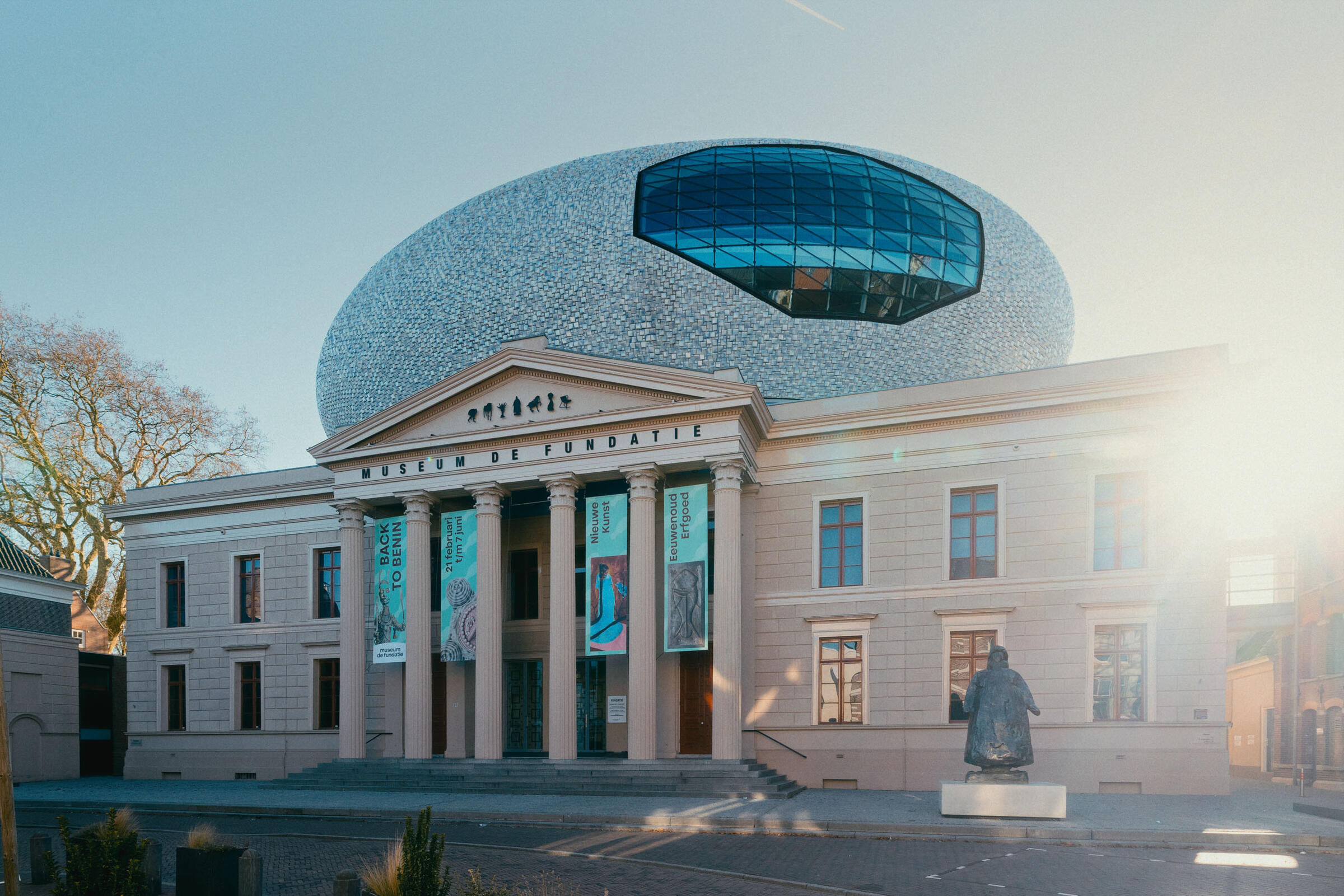 Eine Frontansicht des Museum de Fundatie mit den S&auml;ulen und dem ovalen Dach, die im Sonnenlicht deutlich zu erkennen sind.
