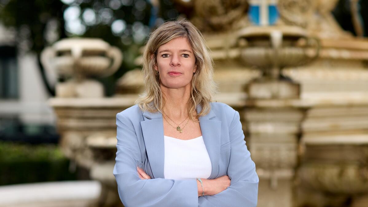 Portretfoto van Rinette van der Vliet. Ze staat met haar armen over elkaar heen geslagen en met een glimlach op de foto.
